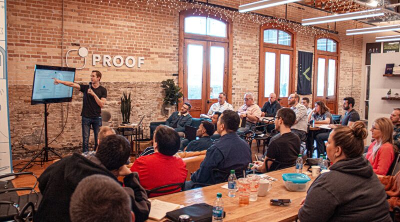 Man presenting to a small group in a brick-walled office, like a pitch to investors