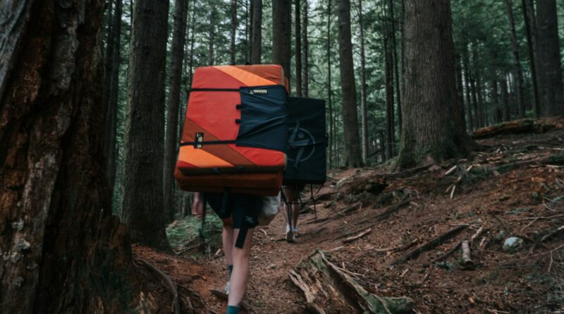 Boulderer with a crash pad walking through woods, relevant to landing safely after a fall