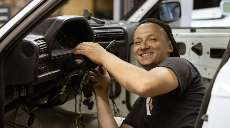 Man in a black t-shirt holding a car steering wheel, relevant to diagnosing steering pull