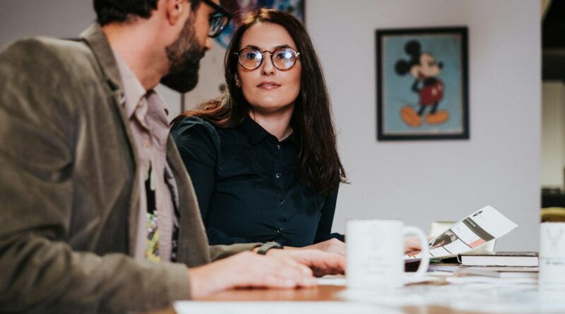 Man and woman sitting at a table together, relating to colleagues supporting one another at work