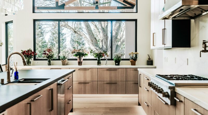 Minimalist kitchen with warm wood cabinetry and large black-framed windows letting in natural light